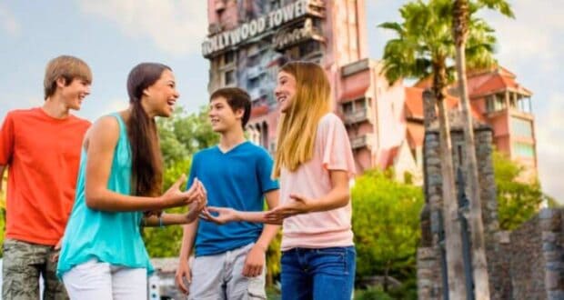 Four teenagers laughing and talking in front of the twilight zone tower of terror attraction in Disney's Hollywood Studios theme park on a sunny day.