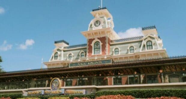 The image captures the entrance to a theme park, reminiscent of Disney magic, with a grand Victorian-style train station and clock tower. Decorative elements stand out against a clear blue sky, while lush landscaping with red flowers adorns the foreground. Nearby, Disney Child Care Services ensures family-friendly fun.
