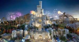 A grand castle with multiple towers stands illuminated against a twilight sky in what feels like a UK-themed Disneyland. Surrounding the castle are amusement park rides, colorful trees, and bursts of fireworks. Flamethrowers create spectacular flames, adding a magical feel to the theme park scene.