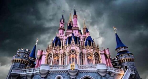 A majestic castle with tall spires and intricate details, illuminated under dramatic dark clouds. The castle is primarily pink with blue rooftops and flags, creating a striking contrast with the stormy sky.