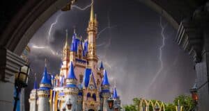 A majestic castle with blue and gold accents stands under a stormy sky with multiple lightning bolts, reminiscent of Disney World's enchanting allure. The scene, framed by a stone archway, creates a dramatic contrast between the vibrant castle and the dark, hurricane-like turbulent sky.