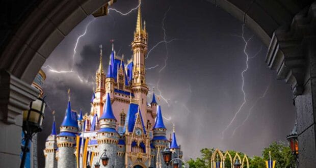 A majestic castle with blue and gold accents stands under a stormy sky with multiple lightning bolts, reminiscent of Disney World's enchanting allure. The scene, framed by a stone archway, creates a dramatic contrast between the vibrant castle and the dark, hurricane-like turbulent sky.