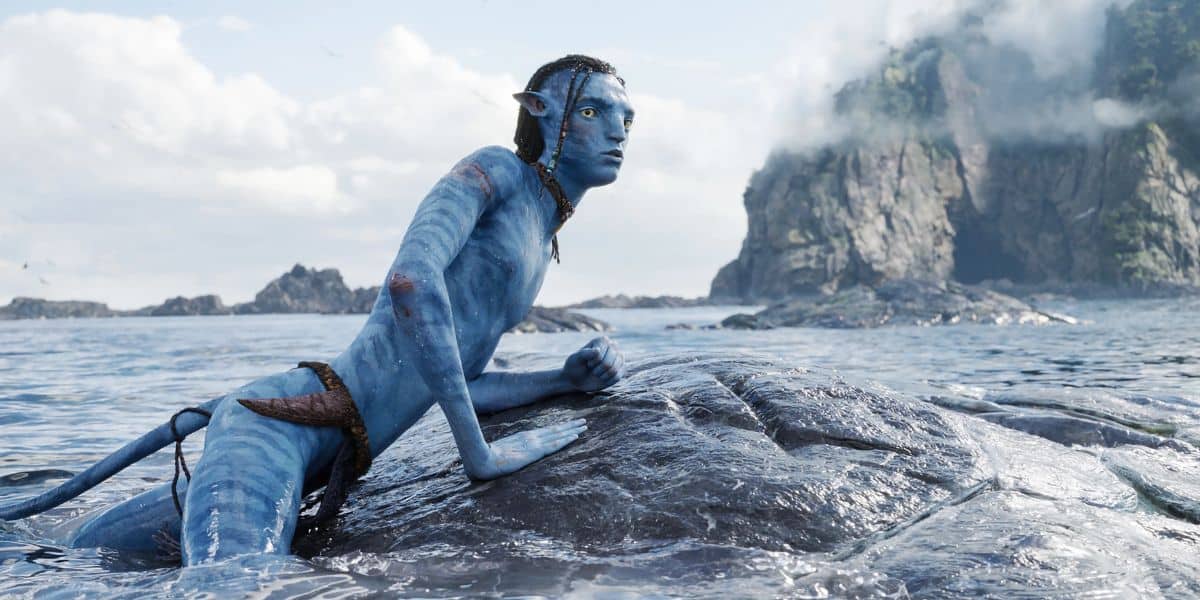 A blue-skinned, humanoid figure resembling an avatar with pointed ears and braided hair is perched on a rock in the ocean.