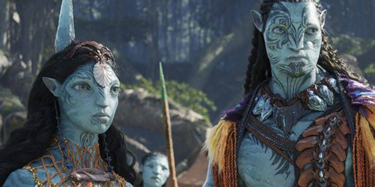 A scene from a fantasy movie features two blue characters with intricate facial markings and traditional attire. They stand in a lush, forested environment, with another similar figure visible in the background.
