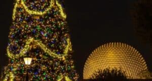 A large Christmas tree adorned with multicolored lights stands illuminated at night next to a glowing geodesic dome structure. The tree is decorated with festive ornaments, and a streetlamp is visible in the foreground.