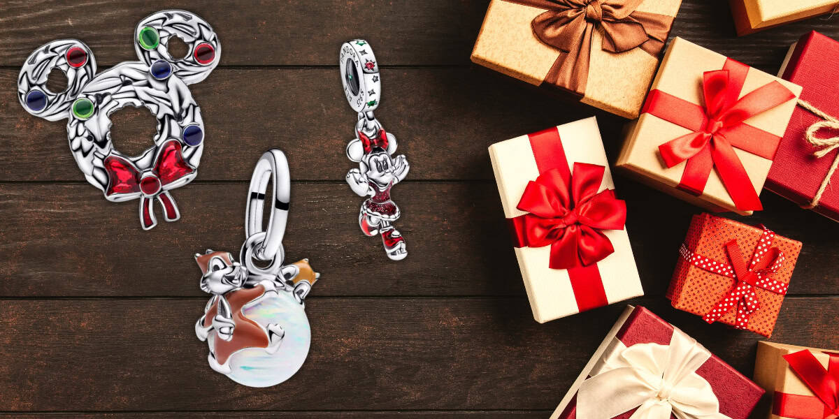 A collection of Christmas-themed charms, including wreaths and festive designs, displayed next to a pile of wrapped gift boxes with red bows, on a wooden surface.