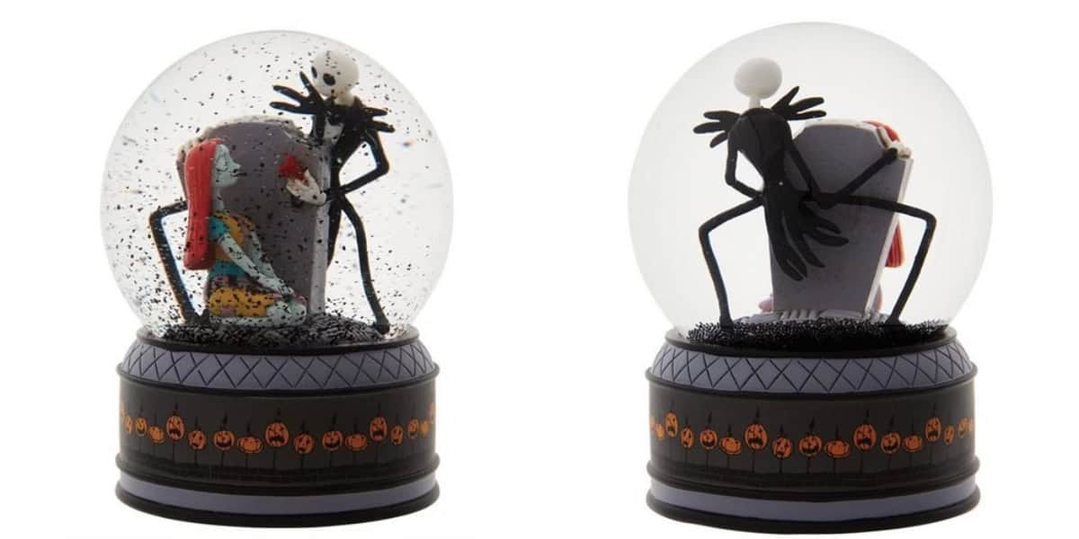 Two snow globes featuring characters from a Halloween-themed animated film. One globe shows a woman with red hair sitting on a gravestone, the other shows a tall figure in black with a bow on a similar gravestone. Both bases have pumpkin designs.