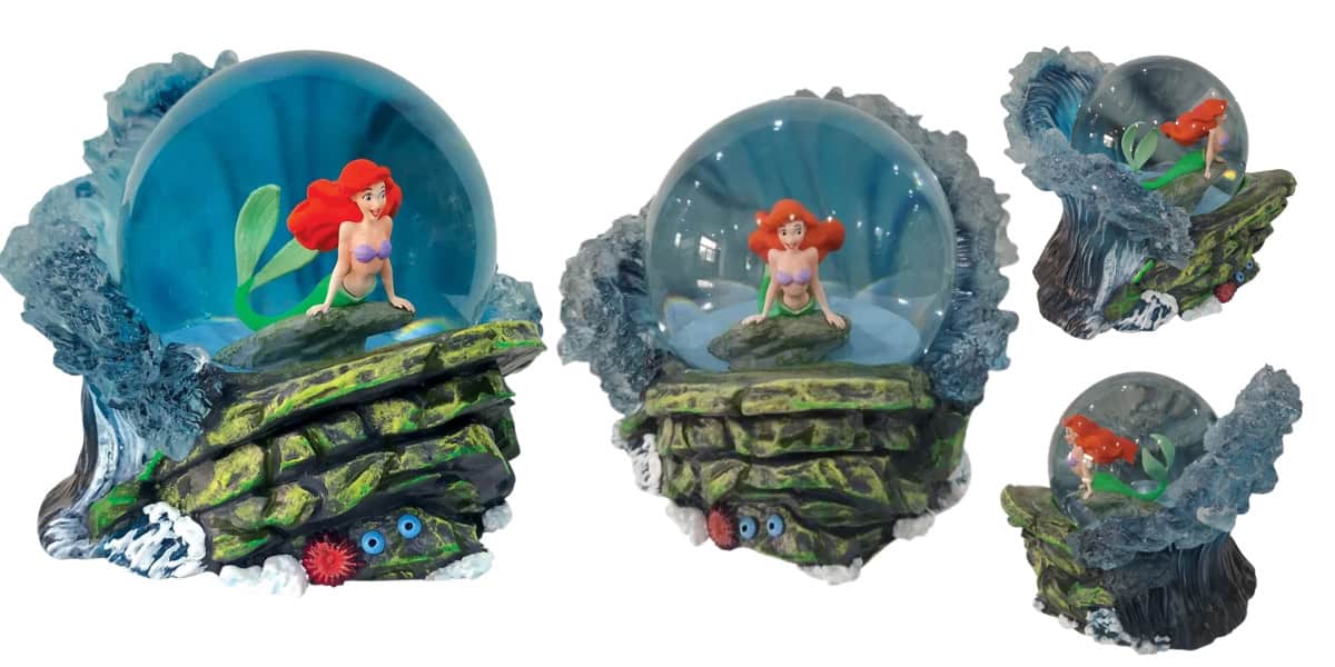 A set of snow globes featuring a red-haired mermaid sitting on a rock with a green tail, surrounded by ocean waves and marine decorations. The mermaid is encased in clear glass domes of varying sizes.