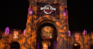 Illuminated entrance of Universal Studios Florida decorated for Halloween Horror Nights 30. The archway displays spooky light patterns and a large circular sign with event details. It is nighttime, enhancing the eerie atmosphere.