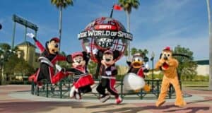 Characters in sports outfits jump in front of the ESPN Wide World of Sports Complex sign. The scene is lively, with palm trees and a clear sky in the background.