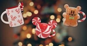 Three Christmas-themed mugs with peppermint and gingerbread designs are displayed against a blurred background of festive holiday lights.
