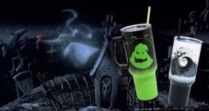 Two Halloween-themed cups with spooky designs are in the foreground. The background features a dark, eerie graveyard scene with a ghostly figure and a gravestone marked "Zero.