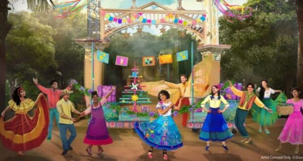 Colorful festival scene with dancers in vibrant traditional costumes performing in front of a decorated stage. Banners, flags, and greenery surround the area, creating a festive atmosphere. People hold baskets and flags, adding to the lively celebration.