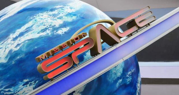 A futuristic sign with the words "MISSION SPACE" in bold letters is mounted diagonally above a large Earth globe backdrop, set within an interior space with a modern design.