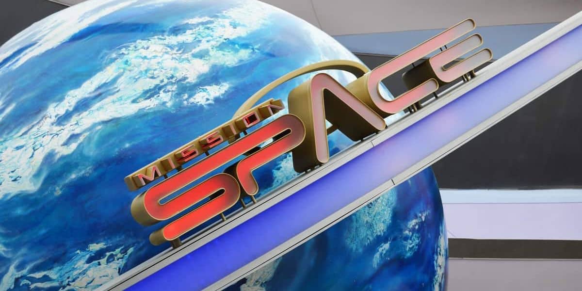 A futuristic sign with the words "MISSION SPACE" in bold letters is mounted diagonally above a large Earth globe backdrop, set within an interior space with a modern design.