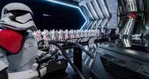 A row of stormtroopers stands inside a futuristic spaceship hangar. A stormtrooper in the foreground has red markings on its armor. The room is metallic and sleek, with a large open bay showing space and a starship.