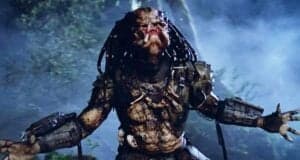 A menacing alien creature with dreadlock-like hair, armored gear, and reptilian skin stands in a misty forest, mouth open in a roar and arms spread wide.