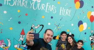 A smiling family of four takes a selfie in front of the Share your ears wall