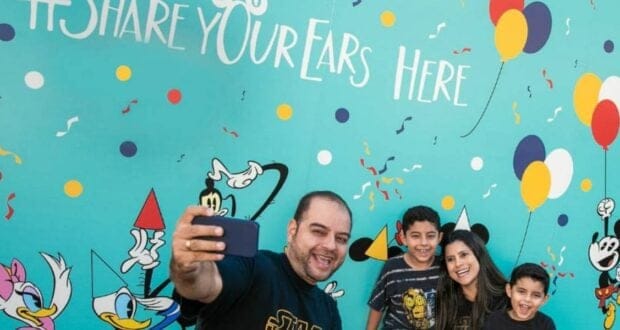 A smiling family of four takes a selfie in front of the Share your ears wall