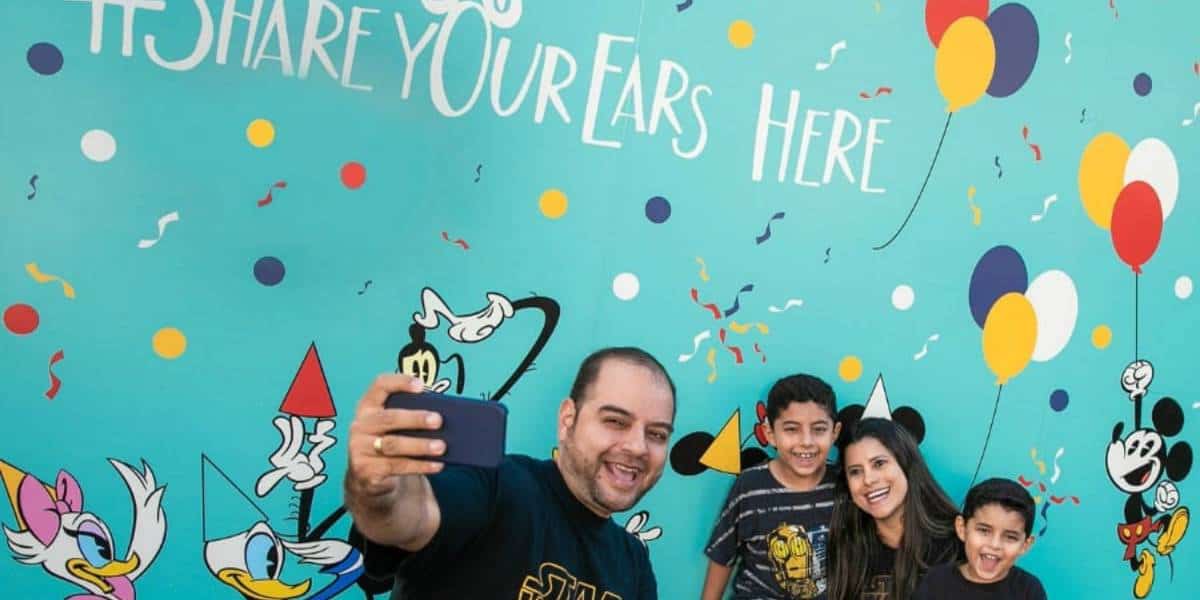 A smiling family of four takes a selfie in front of the Share your ears wall