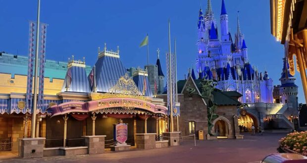 Fantasyland in Magic Kingdom at dusk, featuring the Princess Fairytale Hall and Cinderella Castle illuminated with purple and blue lights. The area appears empty and peaceful.