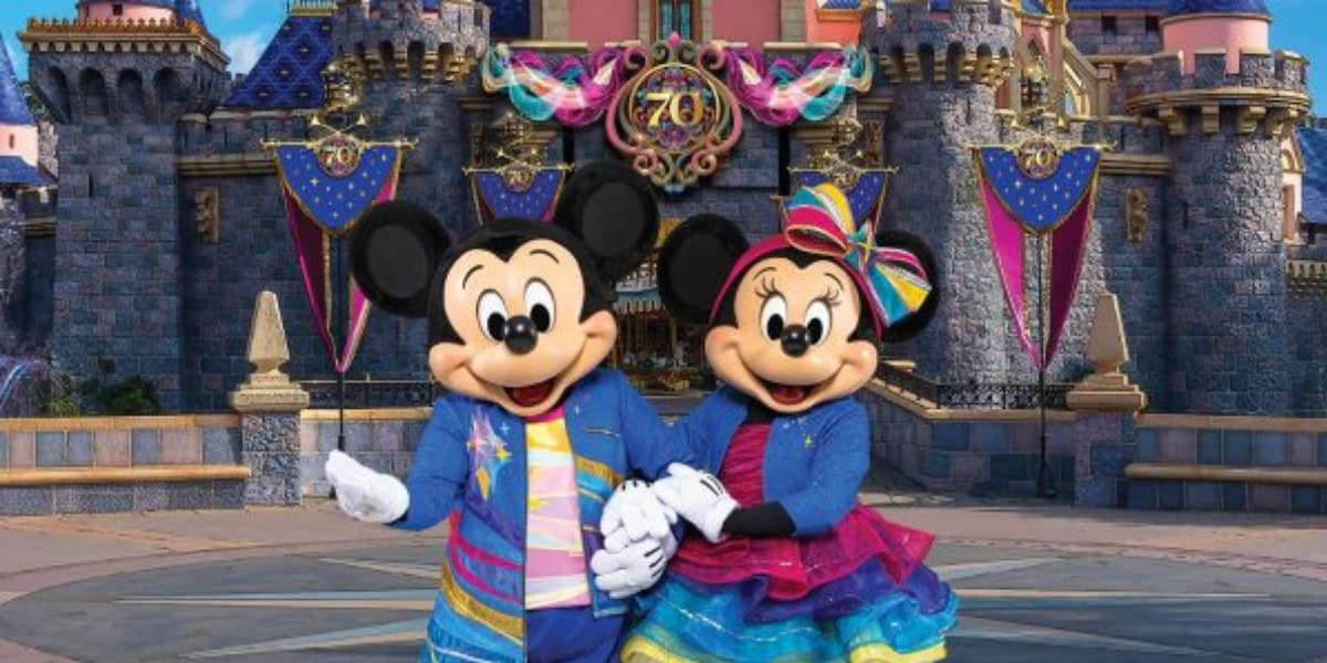 Mickey Mouse and Minnie stand in front of a castle adorned with Disneyland70 decor.