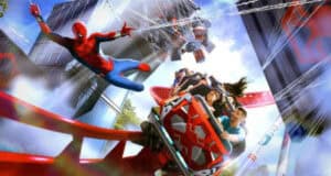 Spider-Man swings above excited riders on a red roller coaster at Shanghai Disney Resort, with webbing and metallic city structures in the vibrant background.