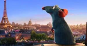 A blue rat with large pink ears sits on a rooftop, gazing at the Paris skyline with the Eiffel Tower in the background at sunset.