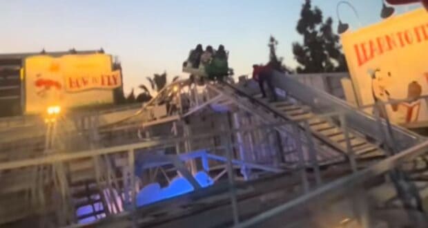 A group of people are stranded in a Goofy's Sky School car at the top of a track, as a person walks up the stairs to assist them