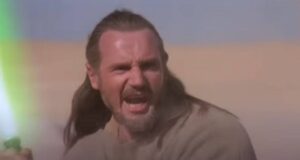 A bearded man with long hair shouts while holding a green lightsaber, standing in a desert landscape under a clear sky.
