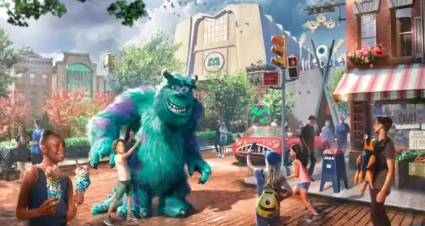 Colorful animated street scene with children and adults interacting with Sulley, a large blue and purple monster from Monsters, Inc., amid whimsical buildings, bright signage, and playful decorations.