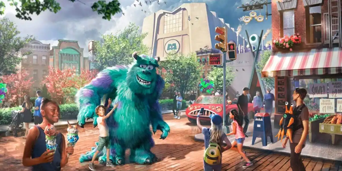 Colorful animated street scene with children and adults interacting with Sulley, a large blue and purple monster from Monsters, Inc., amid whimsical buildings, bright signage, and playful decorations.