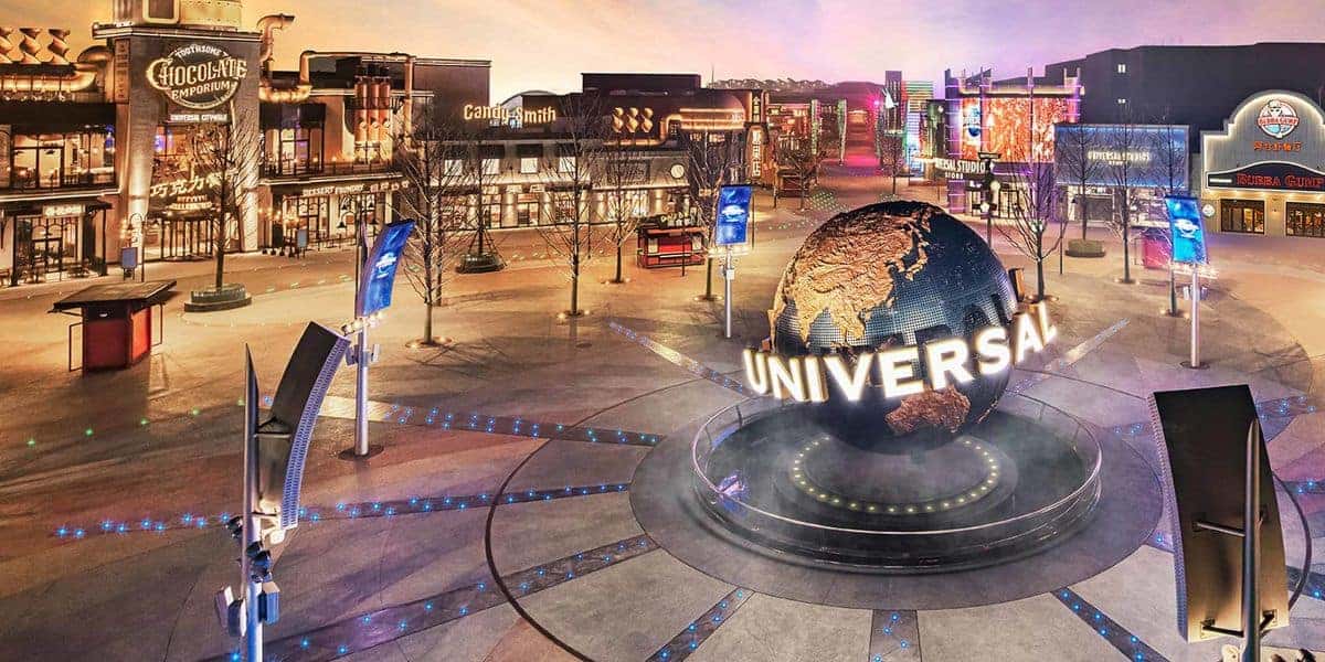A large rotating globe with the word "Universal" stands at the center of a plaza at Universal CityWalk, surrounded by shops, restaurants, colorful lights, and banners in an urban entertainment district at dusk.