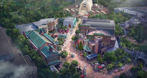 Aerial illustration of a theme park area with colorful buildings, tree-lined streets, pathways, a central fountain, and people walking. In the background, large structures and greenery surround the vibrant scene.