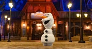 Olaf greets guests with open arms outside a glowing nighttime venue, spreading Frozen magic to everyone at the park.