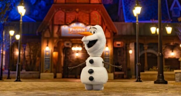 Olaf greets guests with open arms outside a glowing nighttime venue, spreading Frozen magic to everyone at the park.