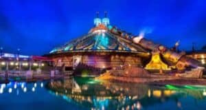 Space Mountain aglow at night, shining over water with a starry sky, as fans await its exciting 2027 refurbishment.