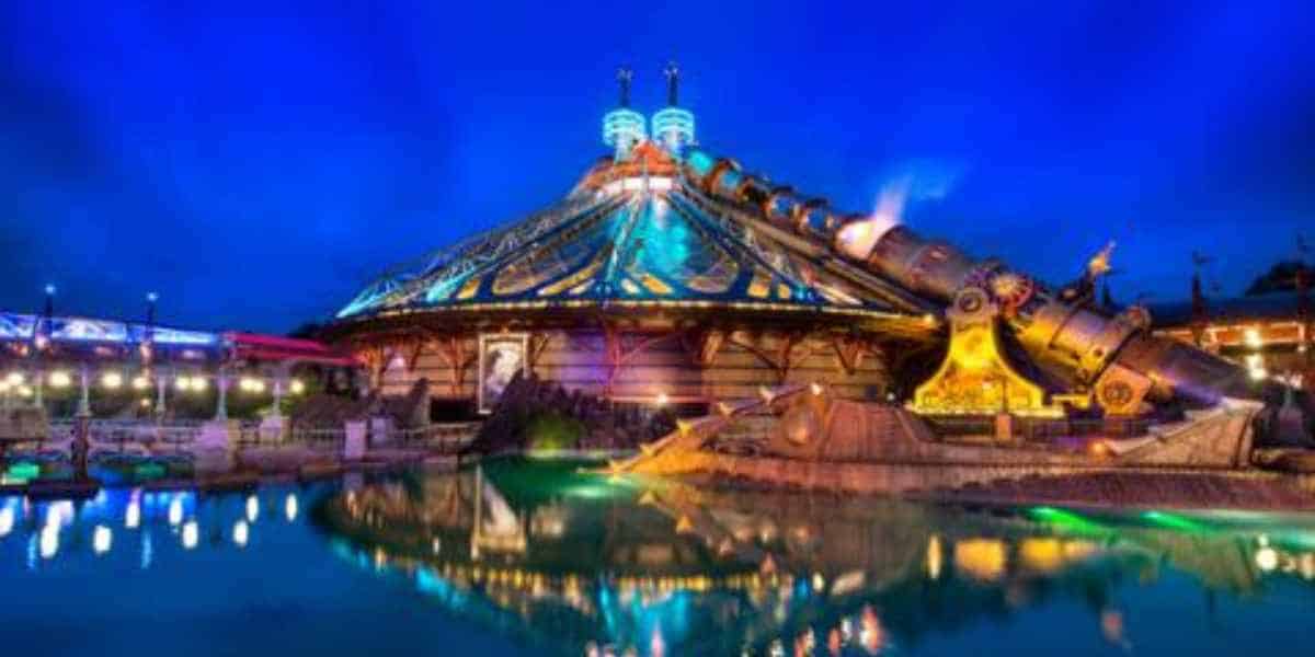 Space Mountain aglow at night, shining over water with a starry sky, as fans await its exciting 2027 refurbishment.