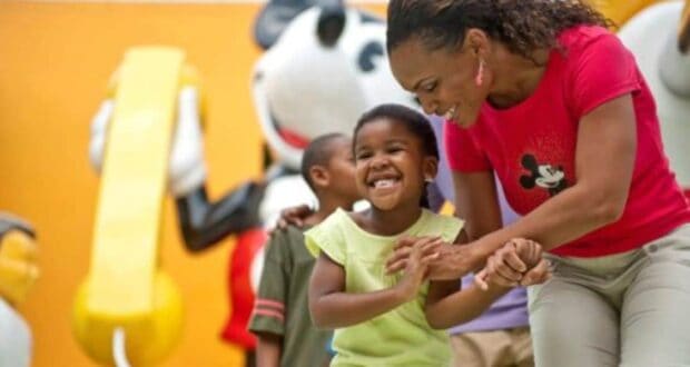 A happy woman and child hold hands near vibrant Disney character statues, as Disney World enforces new vendor policies.