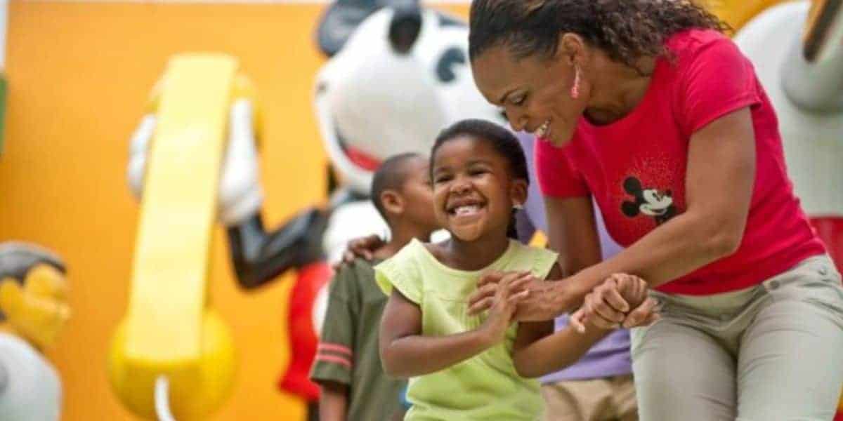 A happy woman and child hold hands near vibrant Disney character statues, as Disney World enforces new vendor policies.