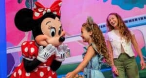 A young guest smiles meeting Minnie Mouse at Disney World, with families enjoying a vibrant park atmosphere in the background.