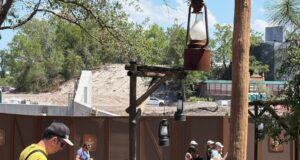 Guests stroll past the Piston Peak construction at Magic Kingdom, with rustic fencing and lanterns dividing it from Big Thunder Mountain.