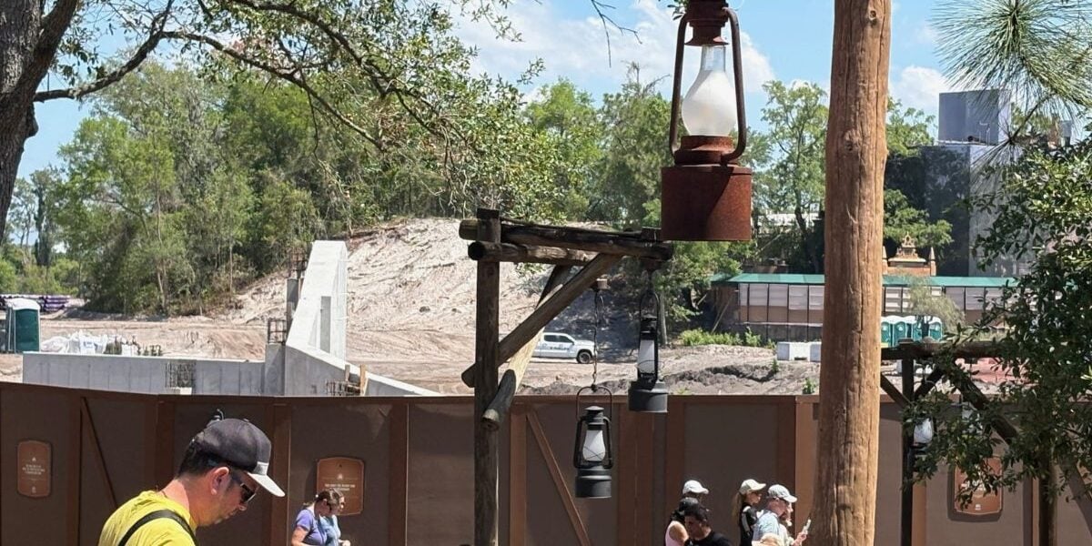 Guests stroll past the Piston Peak construction at Magic Kingdom, with rustic fencing and lanterns dividing it from Big Thunder Mountain.