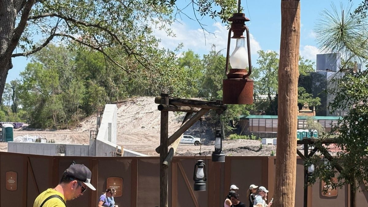 Guests stroll past the Piston Peak construction at Magic Kingdom, with rustic fencing and lanterns dividing it from Big Thunder Mountain.