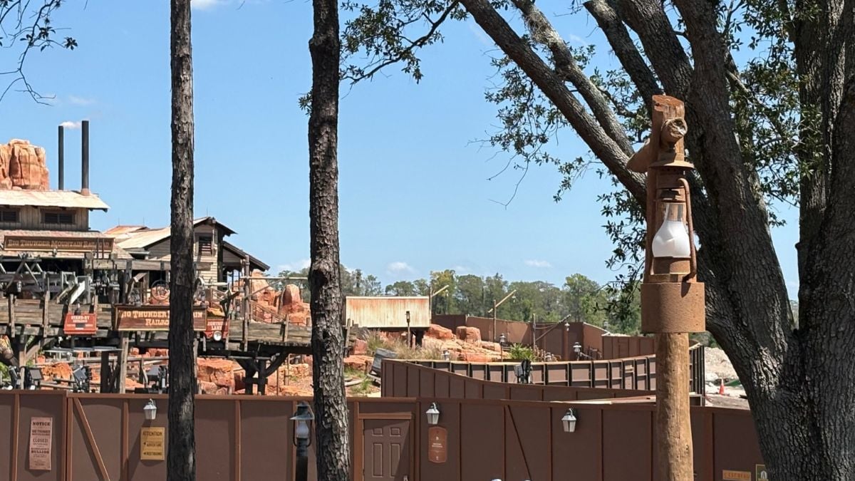 Piston Peak construction at Magic Kingdom, fences and trees, new walls rising by Big Thunder Mountain Railroad, clear blue sky.