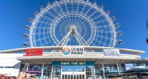 ICON Park’s vibrant entrance in Orlando boasts its iconic Ferris wheel, buzzing with excited visitors beneath clear blue skies.