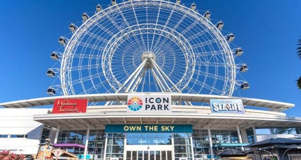 ICON Park’s vibrant entrance in Orlando boasts its iconic Ferris wheel, buzzing with excited visitors beneath clear blue skies.