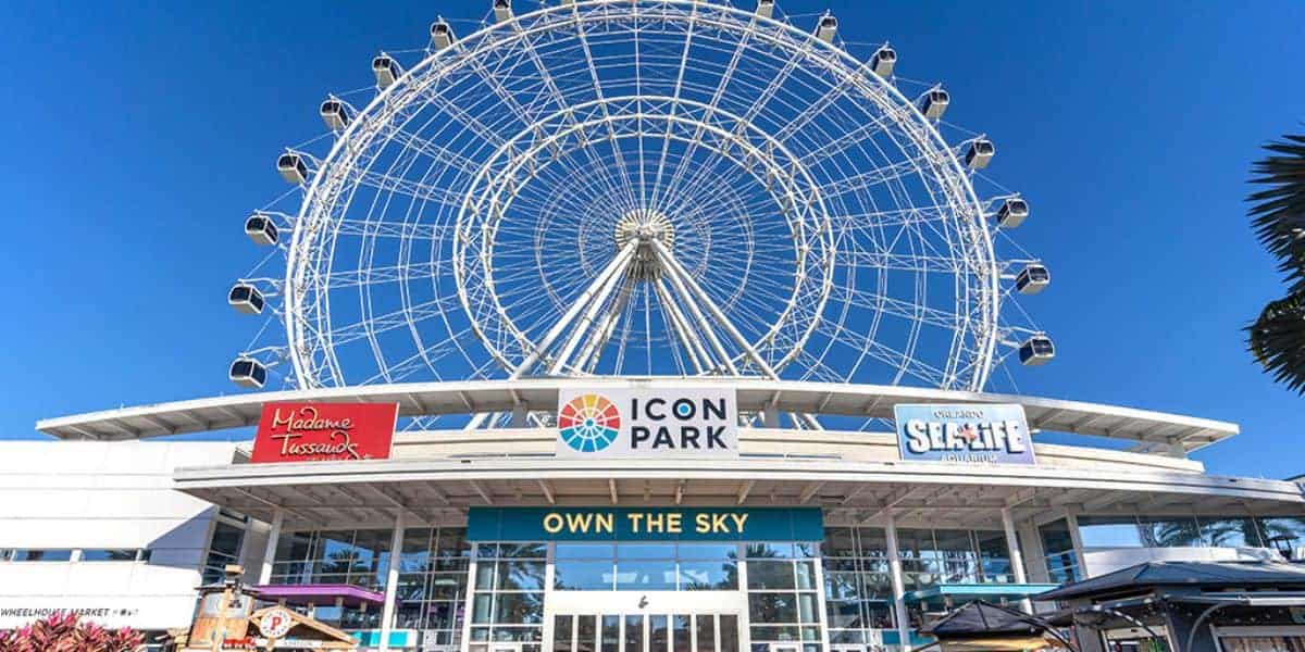 ICON Park’s vibrant entrance in Orlando boasts its iconic Ferris wheel, buzzing with excited visitors beneath clear blue skies.
