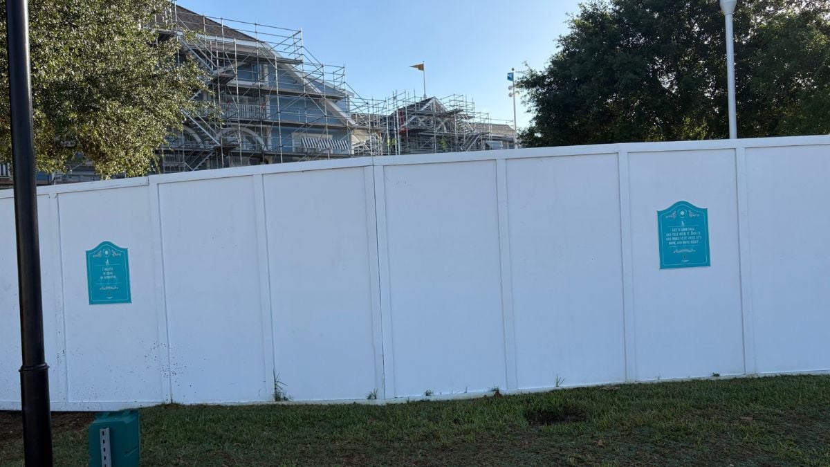 Construction fence with teal signs blocks Beach Club Resort; scaffolding and trees peek over as refurbishment continues at Disney.
