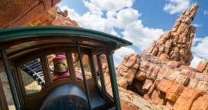 Guests enjoy a thrilling train adventure racing by vibrant red rocks beneath a bright, cloud-dotted sky at the theme park.